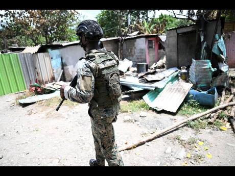 A JDF soldier walks by the burnt remains of a house in Walkers Avenue, Gregory Park. A number of houses were set on fire allegedly by gang members.