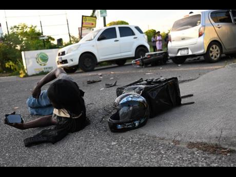 In this file photo, a motorcyclist clutches his cell phone as he lies on the road following a collision in Portmore, St Catherine, 