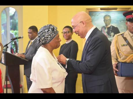 Governor General Sir Patrick Allen (right), pins the Medal of Honour on the lapel of former King’s House staff member, Joy Scott, at the awards ceremony held on September 28 at King’s House.