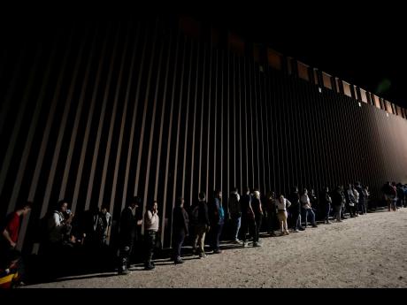 People line up against a border wall as they wait to apply for asylum after crossing the border from Mexico on July 11, 2023, near Yuma, Arizona.