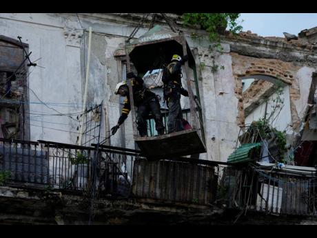 Firefighters stand in a cage, held by a crane, as they search for survivors after a building partially collapsed in Havana, Cuba, Wednesday, October 4, 2023. 
