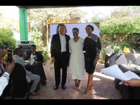 Attorney-at-law M. Georgia Gibson Henlin is sandwiched by Prime Minister Andrew Holness and his wife, Speaker of the House Juliet Holness, shortly after his presentation.