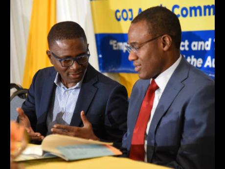 Bruce Scott (left), territory leader/senior partner, PWC Jamaica, leafs through a copy of his book  ‘14 Steps to Financial Freedom’ with Dr Nigel Clarke (right), minister of finance and the public service, during the Audit Committees’ Conference 2023