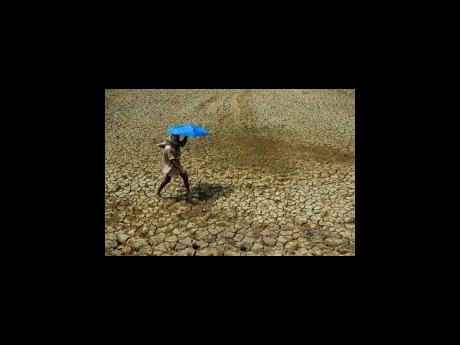 Credit: AP A villager holding an umbrella to protect himself from the sun, walks over parched land on the outskirts of Bhubaneswar, India in 2009. Tense negotiations at the final meeting on a climate-related loss and damages fund – an international fund to help poo