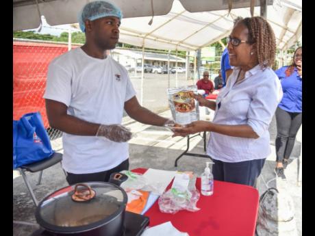 Credit: Nicholas Nunes/Photographer Prep2Pot representative Gavin Dixon (left) hands Faith Webster a pre-prep jerk chicken sample, along with a package of the product, at the SRC Exhibition on Thursday.
