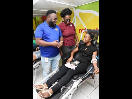 Jamar Howell, chairman of the JN Sports and Social Club, and Toni Moy Stewart, immediate past president of the Rotaract Club of Kingston (RCOK), speak with rotaractor Shari Watson (seated) as she prepares to donate blood at the 2022 staging of the RCOK’s
