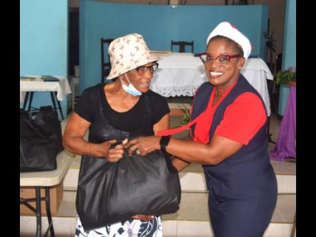 Credit: Contributed SAJ internal auditor Jeans Hinds-Bell (right), presents a care package to a resident during the company’s Christmas treat.