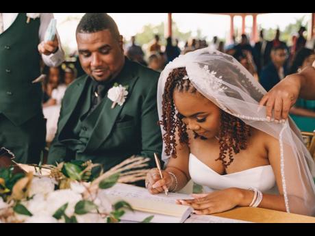Credit: Contributed With an acknowledging grin, the groom gazes fondly as his bride seals their love into the parchment of forever.