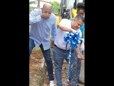 Minister without Portfolio in the Ministry of Economic Growth and Job Creation, Senator Matthew Samuda (right), turns on the pipe in Lime Bottom, St. Ann, on December 22, while Councillor for the Ocho Rios Division, Michael Belnavis, drinks some of the liq