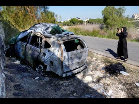 A woman takes pictures of a burned and damaged car that was used by the senior Hezbollah commander Wissam Tawil, who was killed on Monday, in Kherbet Selem village, south Lebanon.