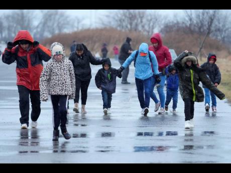 Migrants run in the rain toward the tent at migrant housing location at Floyd Bennett Field, Tuesday, January 9, 2024, in New York. New York City will evacuate the nearly 2,000 migrants housed in tents at the site because of an impending storm. 