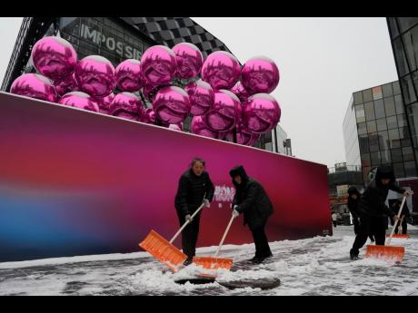 Workers sweep snow into a manhole near a decoration setup ahead of the Christmas festival at a mall in Beijing, on December 14, 2023. China’s exports grew slightly for a second consecutive month in December even as deflationary pressures continue, accord