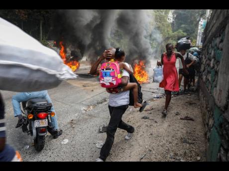 People walk past burning tires during a protest against Haitian Prime Minister Ariel Henry in Port-au-Prince, Haiti, on Monday, February 5.