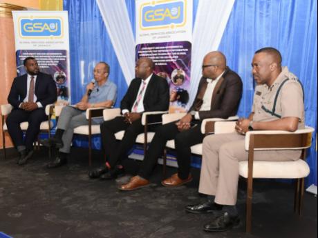 Credit: Contributed Senior Superintendent of Police Vernon Ellis (right) looks on as Dr Horace Chang (second left), minister of national security, addresses the audience during the Global Services Association of Jamaica President’s Breakfast Forum at the Grand-A-View Event