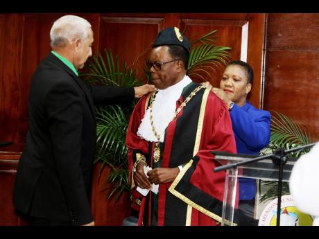 Clarendon Municipal Corporation Winton Maragh, councillor of the Rocky Point division and former mayor of May Pen, is assisted by Nidine Lopez, acting director of administration at the Clarendon Municipal Corporation (CMC), to robe Joel Williams, councillo