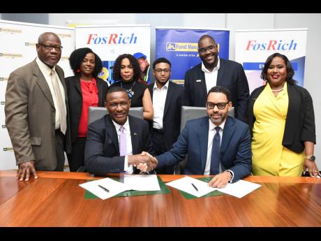 Cecil Foster (sitting at left), chief executive officer of FosRich Company Ltd, shakes hands with Brando Hayden (sitting at right), managing director of JN Fund Managers Ltd following a signing agreement to formalise the successful execution of $900 millio