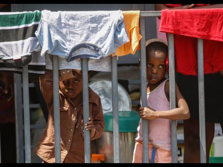 Children look through a fence at a shelter for families displaced by gang violence, in Port-au-Prince, Haiti.