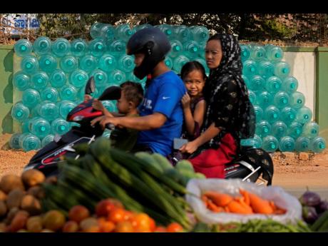 A motorist rides with his family past the stacked empty drinking water cans to be transported for refilling in Bengaluru, India.