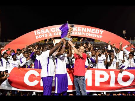 Don Wehby (right), Group Chief Executive Officer of sponsors GraceKennedy Limited, presents the championship trophy to the Kingston College team at the National Stadium last Saturday night.