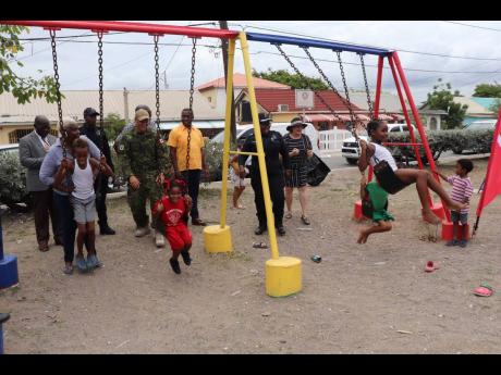 Children enjoy the swing at the renovated park as Lieutenant-Colonel Kevin Doubrough (fifth left), commanding officer of the operation support hub, Superintendent Tomilee Chambers (second right, at back), commanding officer east division (including Port Ro