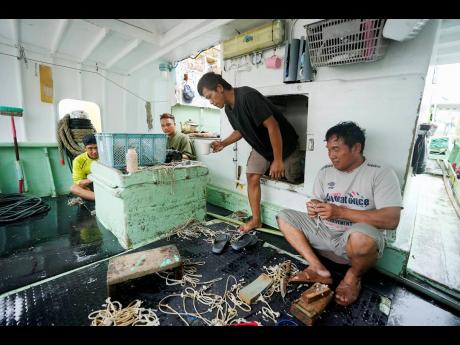 Foreign helpers do some maintenance work on their fishing tools while sitting on their boat docked at the Tomari fishery port in Naha in the main Okinawa island, southern Japan, on June 1, 2023. 