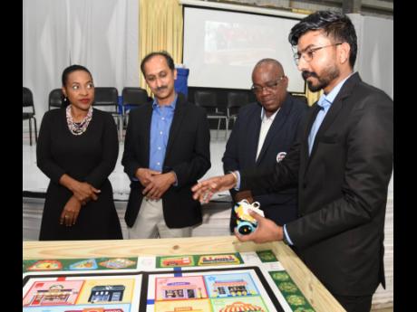 Vikramjeet Singh (right), from Zebra Robotics in Canada, explains how a robot operates on the board once it is programmed properly to Marsha Smith (left), minister of state in the Ministry of Education and Youth, during the official launch of a robotics su