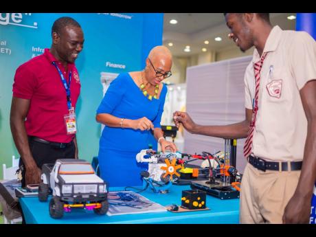 Fayval Williams, minister of education and youth, eagerly engages with a robotics demonstration as she is guided by representatives from the Herbert Morrison Technical High School at the Jamaica Diaspora Conference.