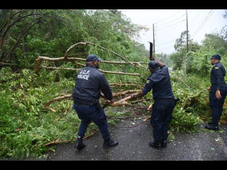 Officers from the Lacovia Police Station clear a blocked roadway after several trees fell during Hurricane Beryl.