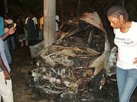 Credit: File A woman views the burnt remains of a Toyota Fielder motor car which crashed in Runaway Bay, St Ann, killing one person several years ago.