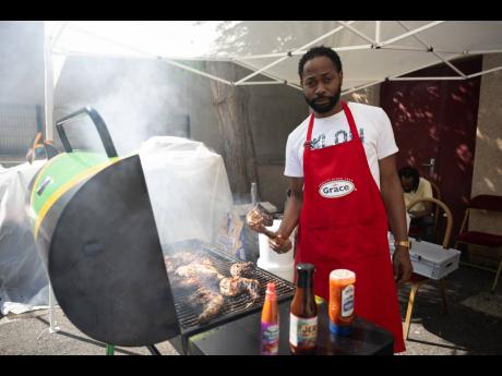 Omar Robinson assists Wayne Smith (not pictured) with preparing jerked chicken outside of Jamaica House to keep the patrons satisfied during their visit on Monday.