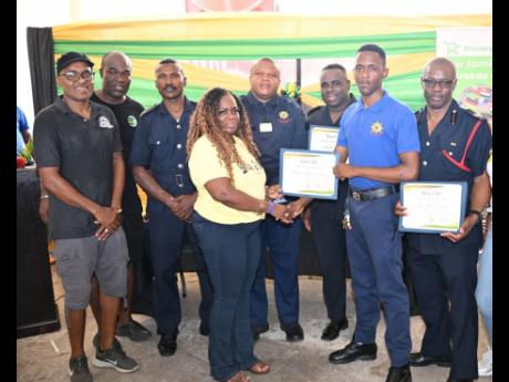 Founder of the Lorraine J. Smith Foundation, Lorraine J. Smith (fourth left), hands over a certificate to firefighter Reinford Brooks (second right), symbolising the adoption of the Jamaica Fire Brigade (JFB) by the Foundation. They are joined by Peter Gra