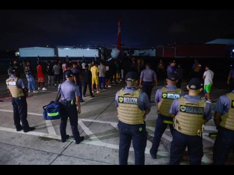 Panamanian immigration agents watch as Colombian migrants prepare to enter a plane as they are deported from Marcos A. Gelabert de Albrook Airport in Panama City yesterday.