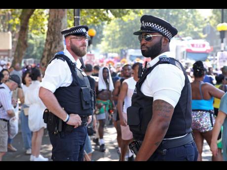 Police patrol as revellers pass by during the Notting Hill Carnival in west London on Monday August 26.  The annual carnival event brings sound systems and dancers parading through the streets surrounding the Notting Hill area of west London. 