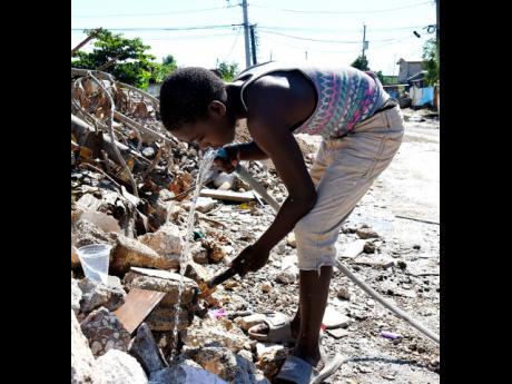 A boy drinks water from a broken pipe along Riverside Drive in New Haven, Kingston.