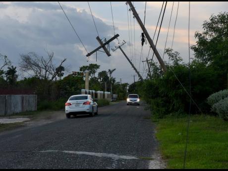 Credit: Ashley Anguin Motorists negotiate their way around lightposts that hang across the main road in Parrottee, St Elizabeth, after Hurricane Beryl in July.