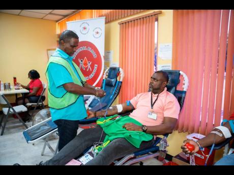 Courtney Brooks, a J. Wray & Nephew Limited staff member, donates  blood with the assistance of team members from the Blood Bank.