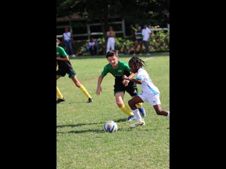 Hillel winger Nugent Walker (right) dribbles away from AISK’s Edward Simon during a Canopy Insurance-JISA U-12 Alberga Cup football match at the National Water Commission’s Mona field on Saturday.