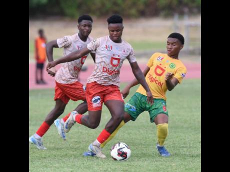 Credit: Ian Allen Denzel McKenzie (centre) of Mona High School dribbles past Chazray Johnson (right) of St Jago High during a Manning Cup round-of-16 match at the Stadium East field on Friday, October 25.