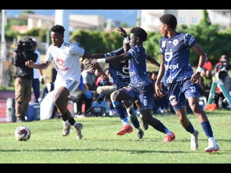 Credit: Ian Allen Denzel McKenzie (left) of Mona High, dribbles past Jamaica College defenders Nashardo Gibbs (second left), Jamarly Bennett (second right), and Dontae Logan (right) during their Manning Cup quarter-final match at the Stadium East field yesterday. The game