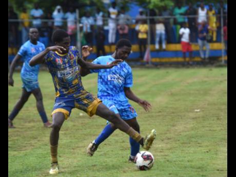 St Elizabeth Technical High School’s Justin McPherson (left) gets between the ball and McGrath High School’s Cliftalleo Mattie during their ISSA/WATA daCosta Cup quarterfinal clash at the STETHS Sports Complex on Saturday.