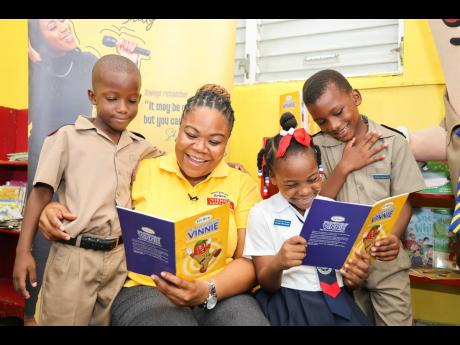 Kadian Parkins (second left), senior brand manager, Grace Foods, reads to grade one students at Franklin Town Primary School (from left), Kenmar Clarke, Denise Wilson, and Tameez Thomas during the official hand over of the Grace Vienna Sausage-powered read