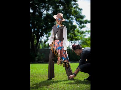 Credit: Adrian Creary Aaliyah Gordon looks on as designer Orlando Sylvister Samuels makes a styling adjustment to her leather pants at a photoshoot on Tuesday in the gardens of The Jamaica Pegasus hotel.
