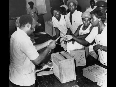 Electors showing enthusiasm in exercising their franchise at a Corporate Area polling station on Wednesday, December 15, 1976. Here, a voter is seen receiving her ballot paper as a group of eager youths look on.