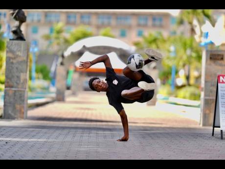 John Manradge acrobatically juggles the ball while balancing on his hand during a freestyle competition at Emancipation Park in New Kingston.