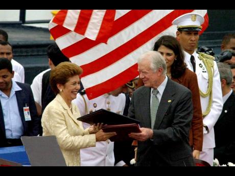 Former President Jimmy Carter (right) exchanges documents with Panamanian President Mireya Moscoso on December 14, 1999, during a ceremony outside Panama City to transfer control of the Panama Canal to Panama, after 85 years of American control, on Decembe