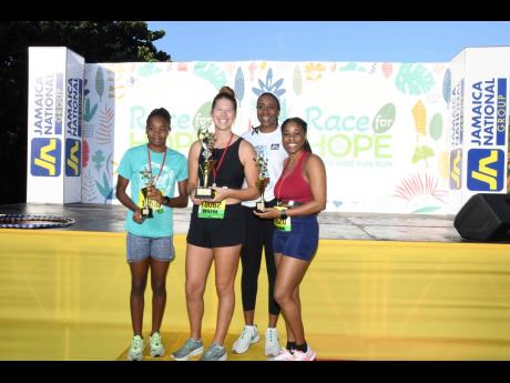 From left: Renae Chung, third-place female runner; Tonya Busse of Pacers Running Club, first-place winner; and Dandie Williams (right), second-place female runner from Pacer’s Running Club, show off their trophies after Josette Smith Scott (back), head o