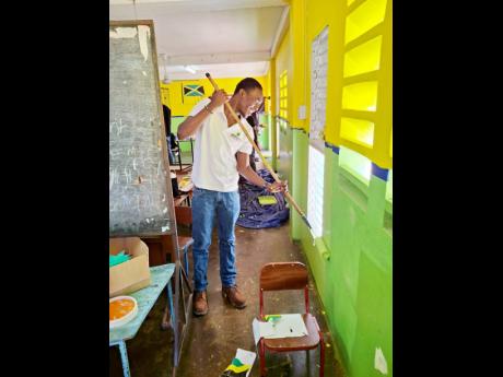 Credit: Contributed Jamalco employee Sean-Dean Hutchinson paints a section of the Comfort Hall Primary School.