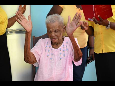 St Thomas centenarian, Eliza Cooper, lifts her hands in reverence as she sings the hymn, ‘Near the Cross’, with members of the Sunshine Senior Citizens Club who paid her a visit on January 15, at her Beckford Town home.