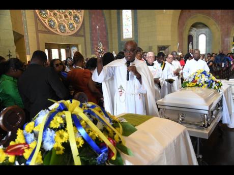 Father Kingsley Asphall sprinkles holy water on the coffins of Camesha and O’Neil Stevens during the funeral service on Saturday.
