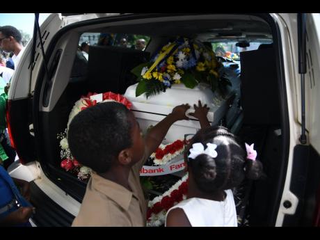 Joseph McLaren (left) and Liana Thompson, grade three students at Jessie Ripoll Primary, rest their hands on coffin of Camesha Lindsay-Stevens, their late principal’s wife, on Saturday.